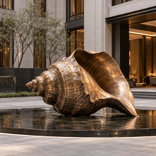Outdoor bronze seashell statue displayed at a luxury hotel entrance courtyard with modern architectural surroundings.