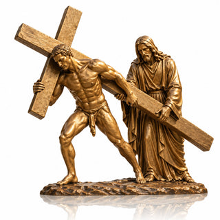 Golden bronze Jesus carrying the cross religious sculpture displayed in a landscaped Catholic church garden.