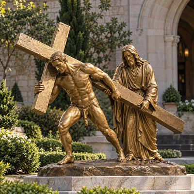 Golden bronze Jesus carrying the cross religious sculpture displayed in a landscaped Catholic church garden.
