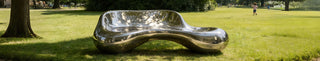 A durable and weather-resistant stainless steel sculpture bench installed in a sunny public park or garden