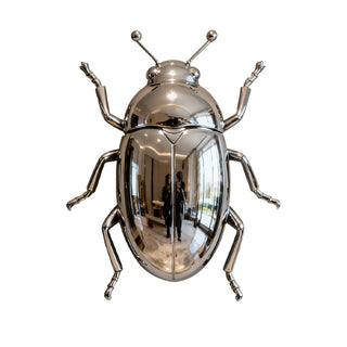 Stainless steel beetle wall sculpture installed in outdoor garden landscape creating modern decorative